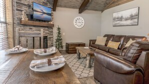 A cozy living room with a stone wall, a fireplace, a leather couch, and a wooden dining table set for four.