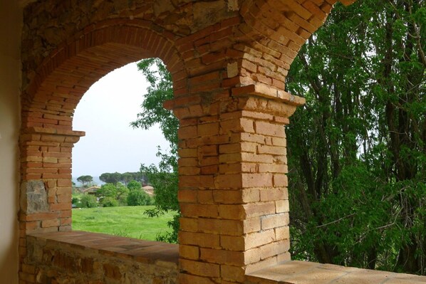 A brick archway with a view of a green landscape and trees.