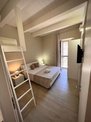 Ein Schlafzimmer mit Etagenbett, Nachttisch mit Lampe, Wandfernseher und einem Fenster mit Vorhängen.