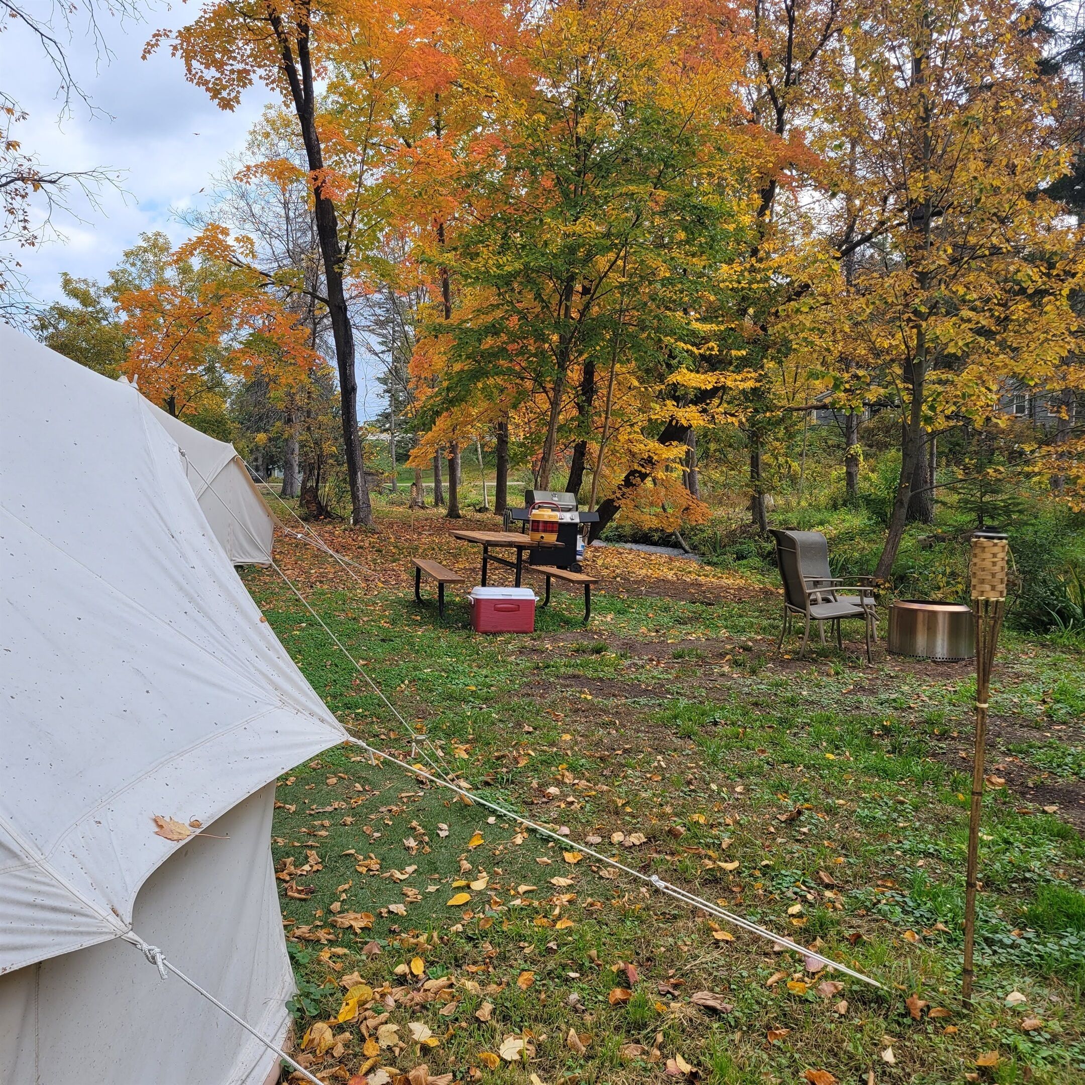 A campsite with a tent, picnic table, chairs, and a cooler.