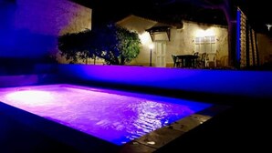 A nighttime view of a swimming pool with purple lighting, a patio area with a table and chairs, and a building with a door and windows. - Gite des écureuils, sea view, private pool, parking, air conditioning (La Ciotat)