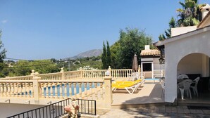 A pool area with a stone floor, a white fence, and a view of a mountain.