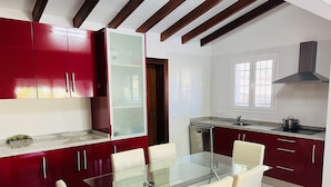 A modern kitchen with red cabinets, a glass dining table, and a dishwasher.