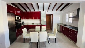 A modern kitchen with red cabinets, a glass dining table, and white chairs.