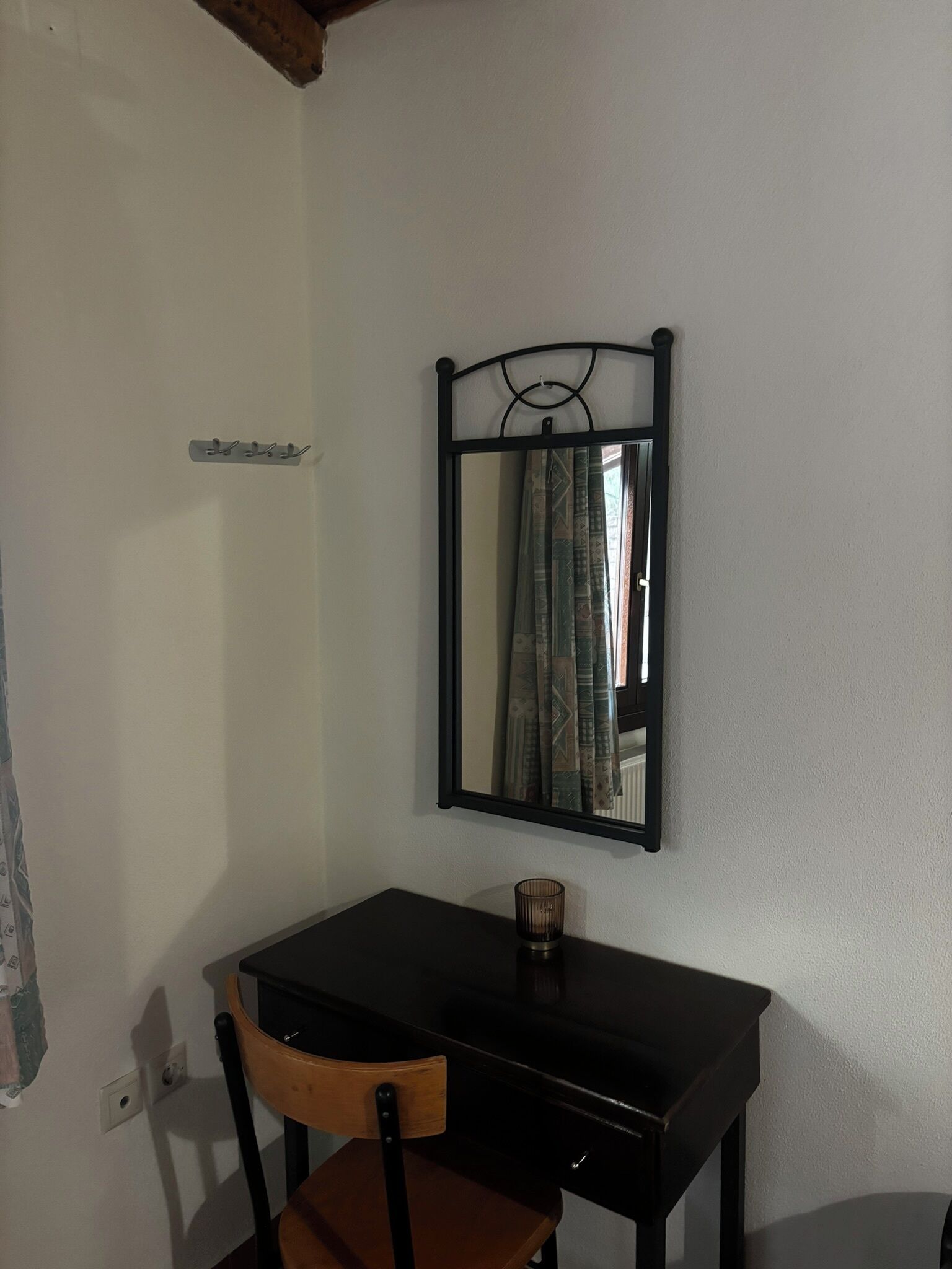Una habitación pequeña con una silla de madera, un escritorio negro y un espejo en la pared.