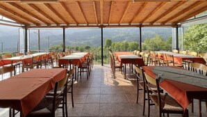 An outdoor dining area with tables and chairs, a wooden ceiling, and a view of mountains.