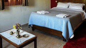 A bedroom with a wooden ceiling, a bed with white linens, a table with a vase of flowers, and a red rug.