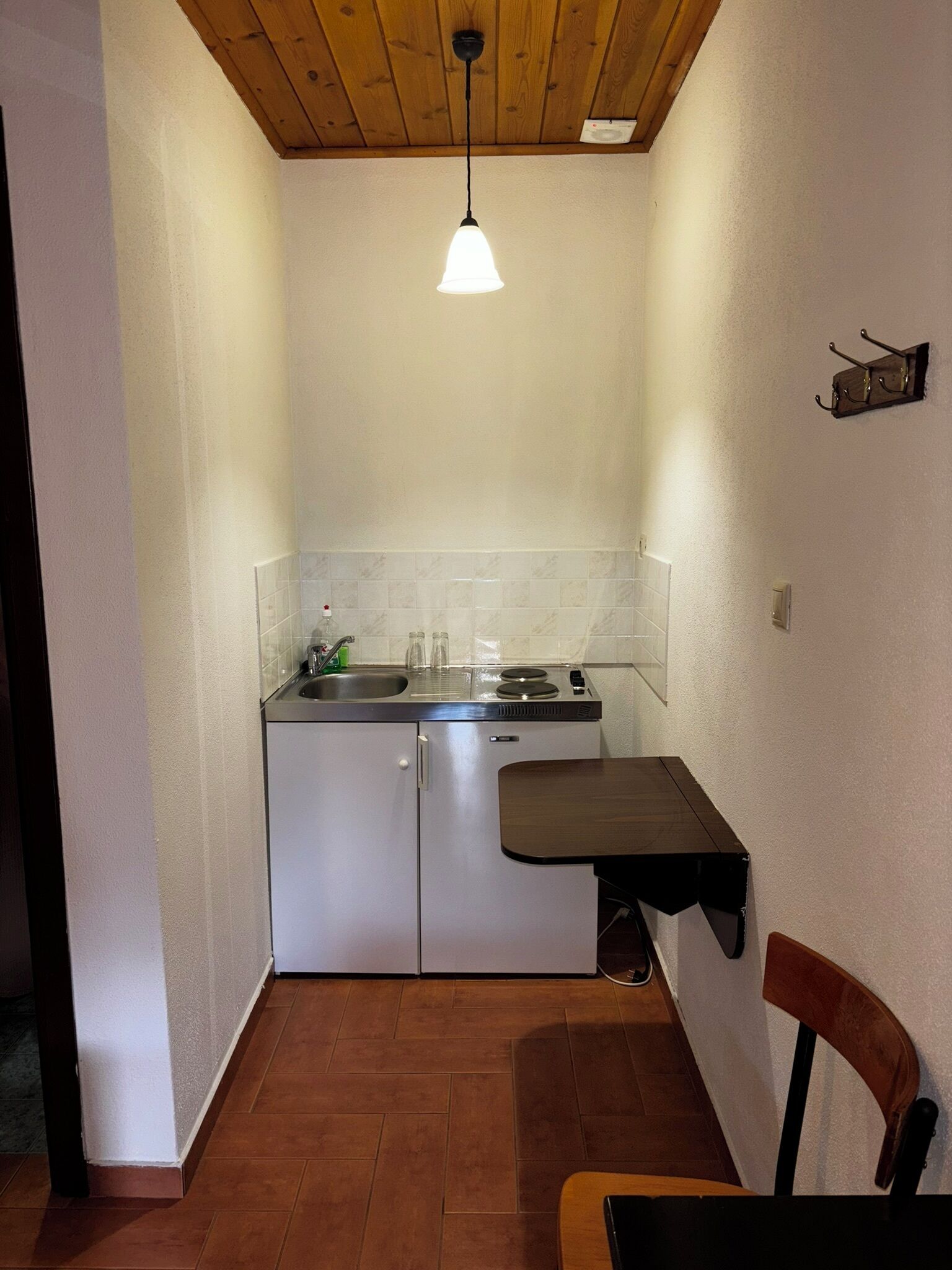 Una cucina compatta con un unico piano di lavoro, un lavandino e un lampadario.