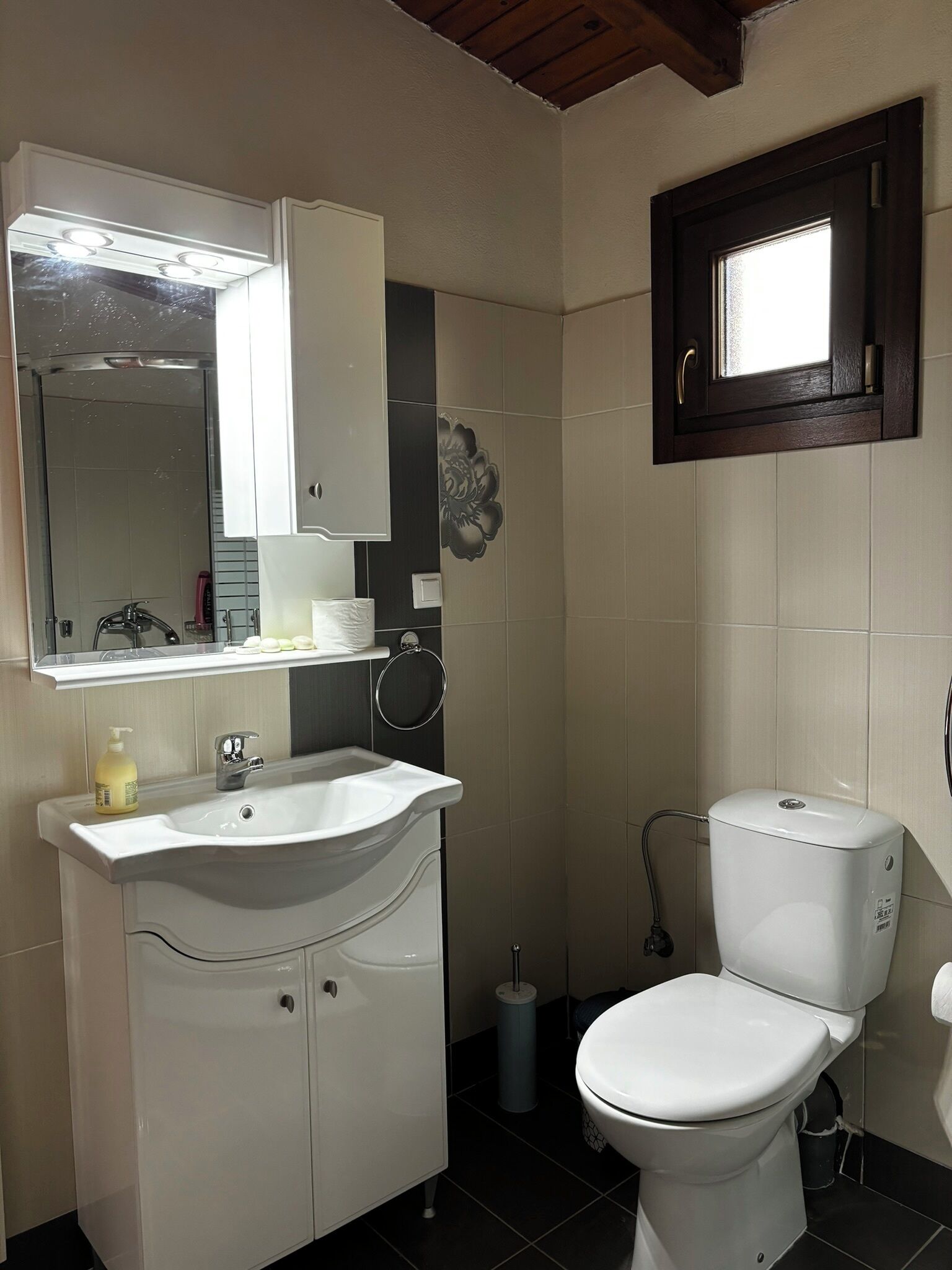 Un baño con lavamanos, espejo e inodoro blancos.