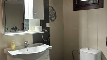 Un baño con lavamanos, espejo e inodoro blancos.