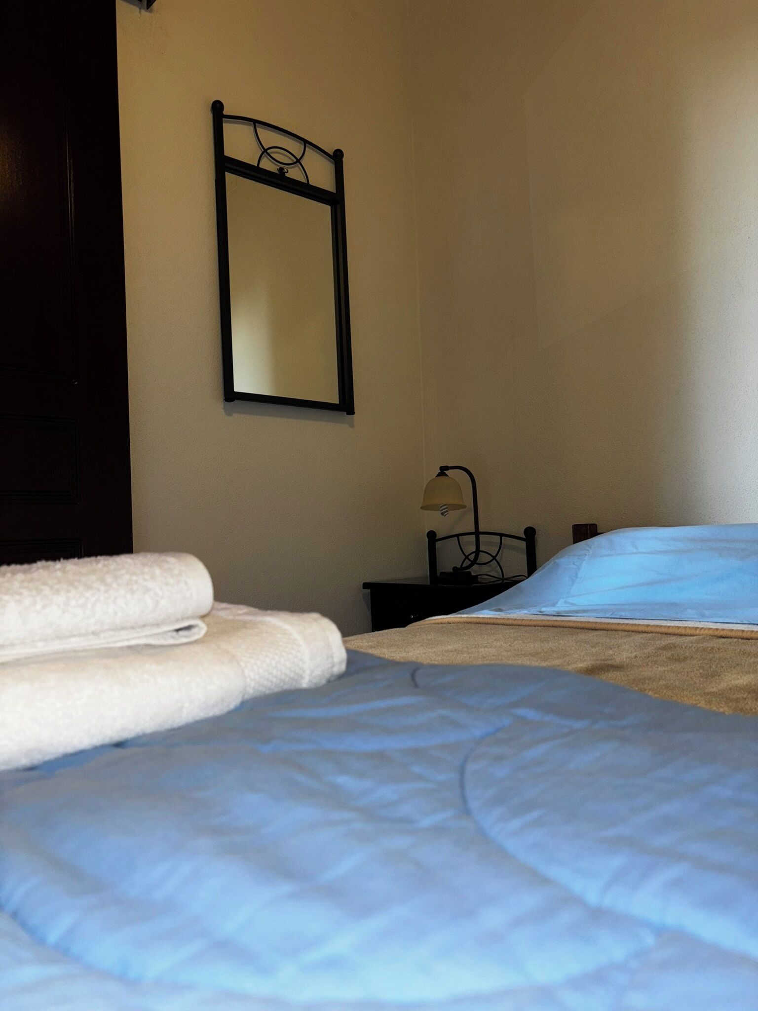 A bedroom with a bed, a nightstand, a lamp, and a mirror on the wall.
