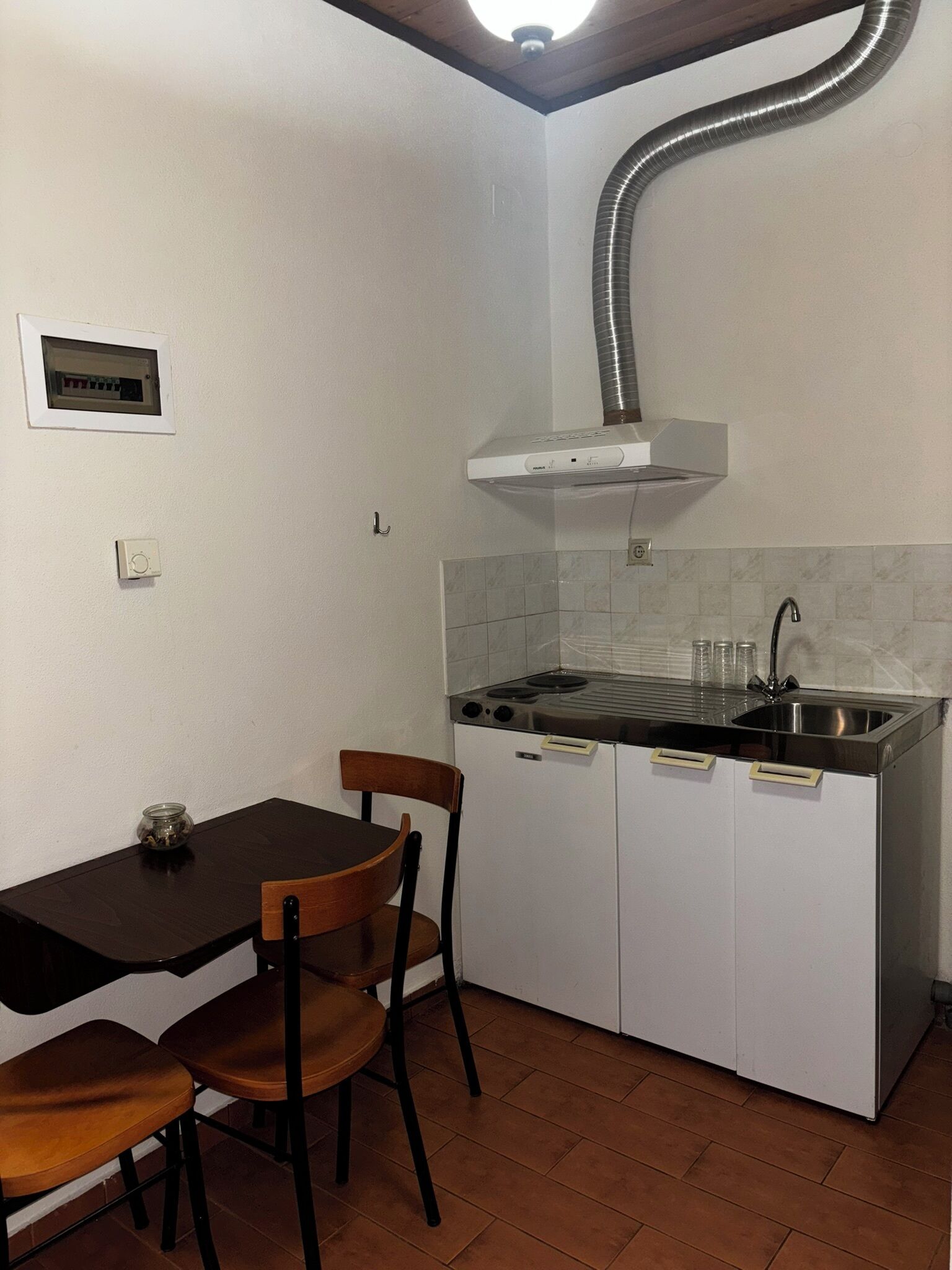 A compact kitchen with a stove, sink, and white cabinets. There is a wooden table with chairs and a small jar on the table.