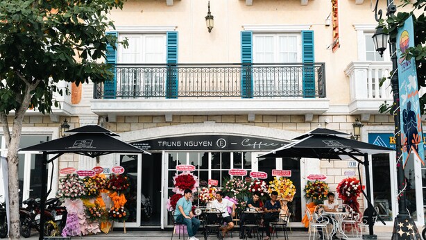 A coffee shop with outdoor seating, a flower display, and a sign reading "TRUNG NGUYEN Coffee". - Royal Hotel Phú Quốc (Phu Quoc)