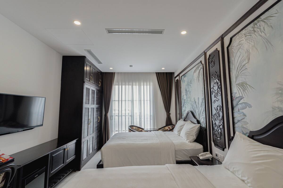 A hotel room with two beds, a flat-screen TV, a minibar, and a large window with curtains.
