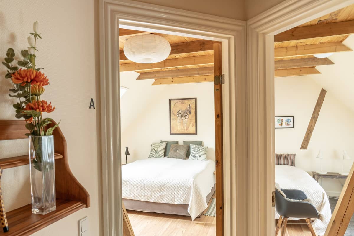 A bedroom with a wooden ceiling, a bed with a white bedspread, and a giraffe figurine on a shelf.