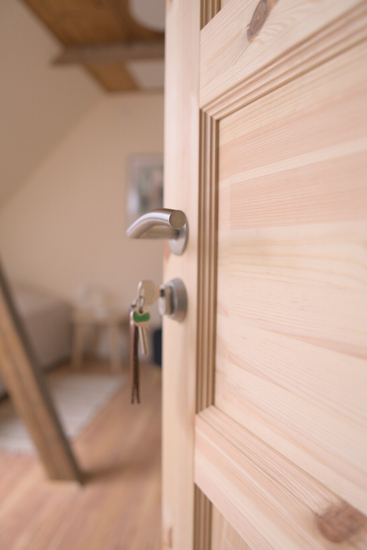 A wooden door with a modern handle and keys hanging on the lock.