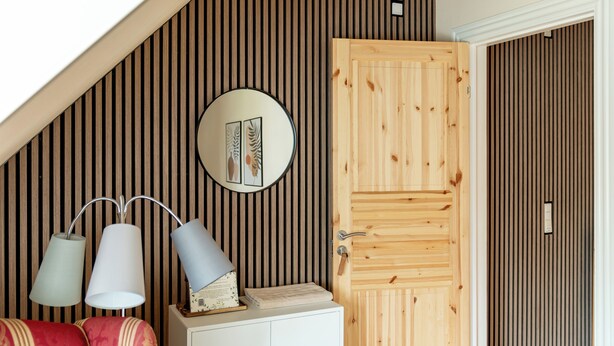 Una habitación con techo inclinado, una puerta de madera, un armario blanco y dos lámparas fijadas a la pared.