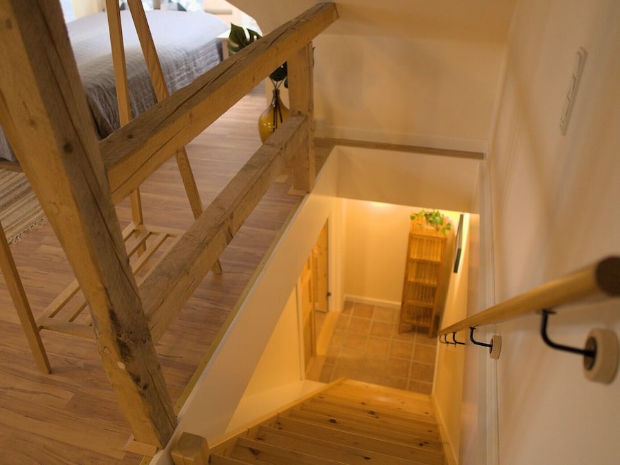 A wooden staircase with a handrail, leading to a room with a bed and a plant.