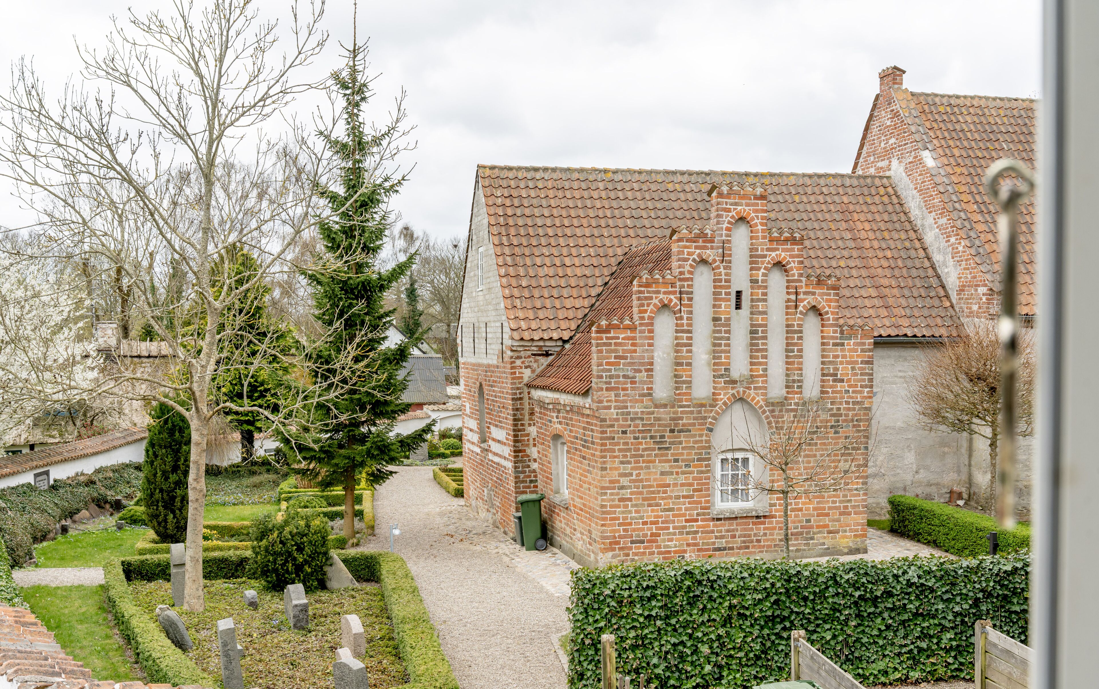 Een historisch bakstenen gebouw met een pannendak, een centraal rondboogvenster en een klein aangrenzend gebouwtje.