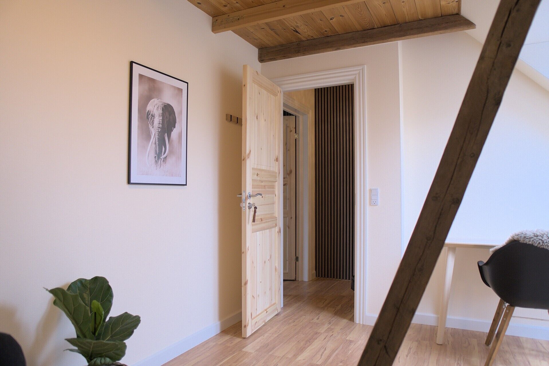 A hallway with a wooden ceiling, a door leading to another room, and a framed picture on the wall.