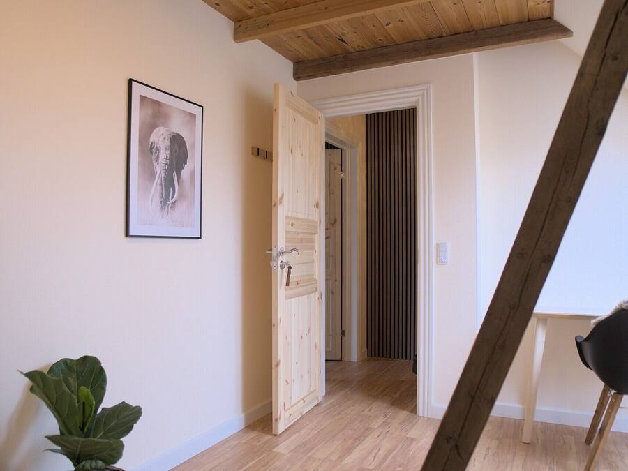 A hallway with a wooden ceiling, a door leading to another room, and a framed picture on the wall.