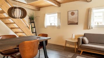 Un comedor con una mesa de madera, sillas de cuero marrón, techo de madera y un sofá gris.