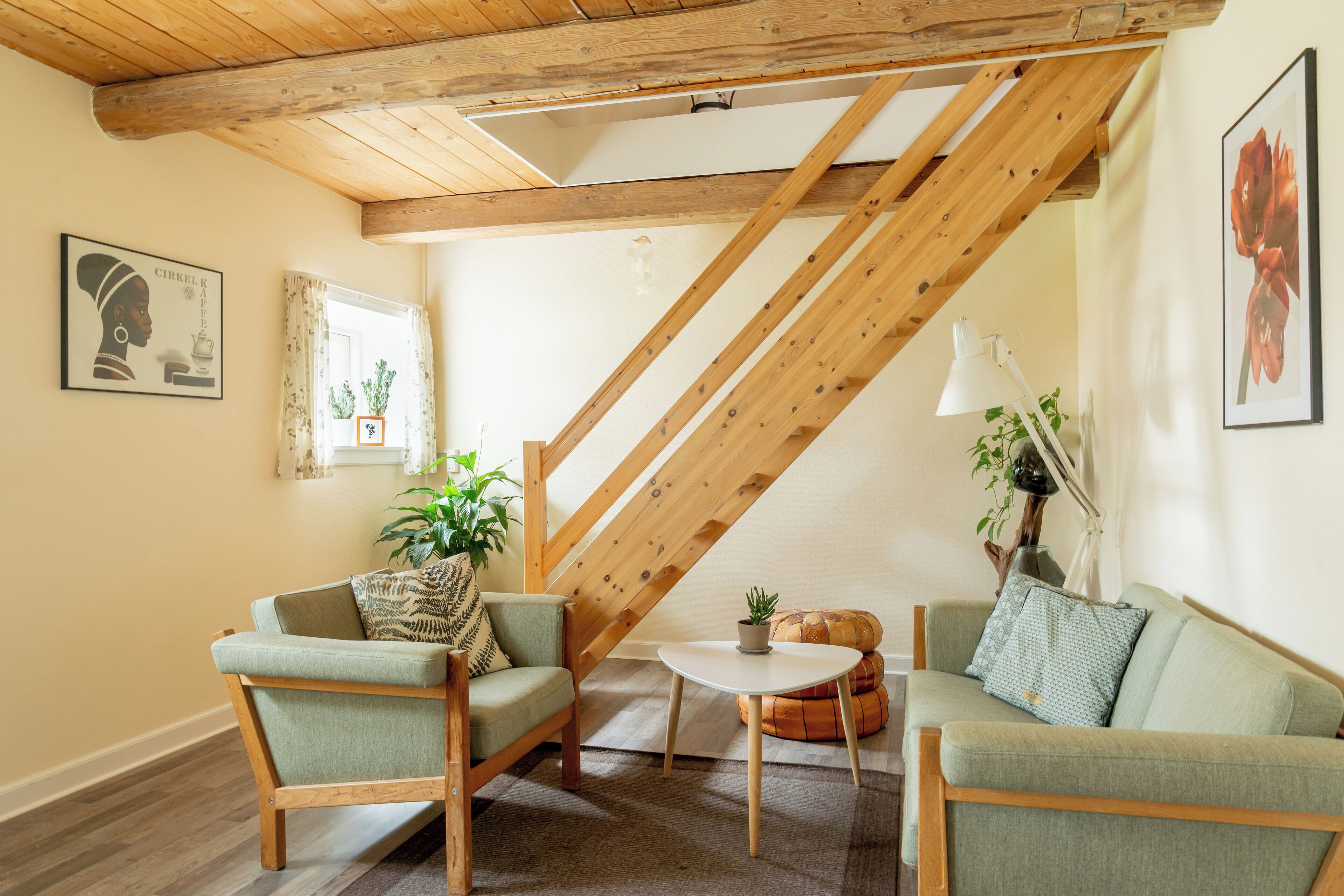 A cozy living room with a high wooden ceiling, a green sofa set, a small round table, and a potted plant.