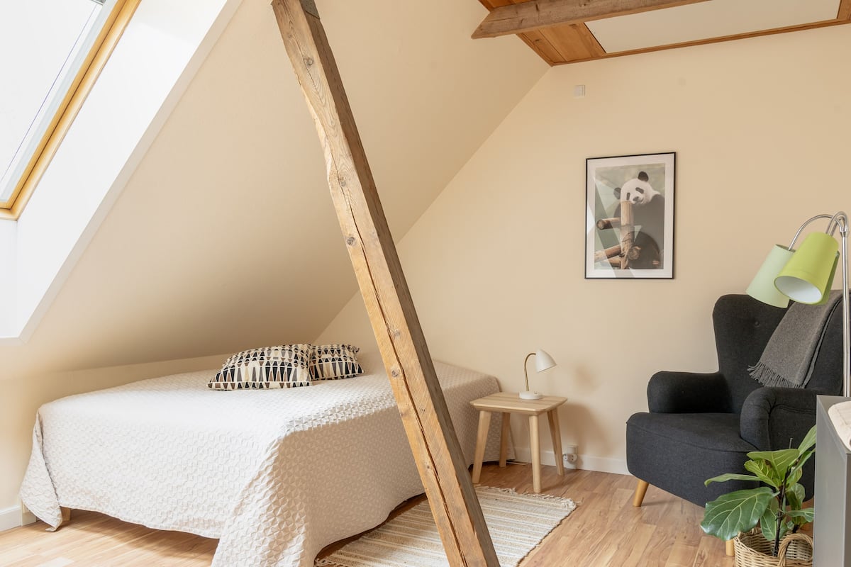 A cozy bedroom with a bed, a chair, a small table, and a lamp.