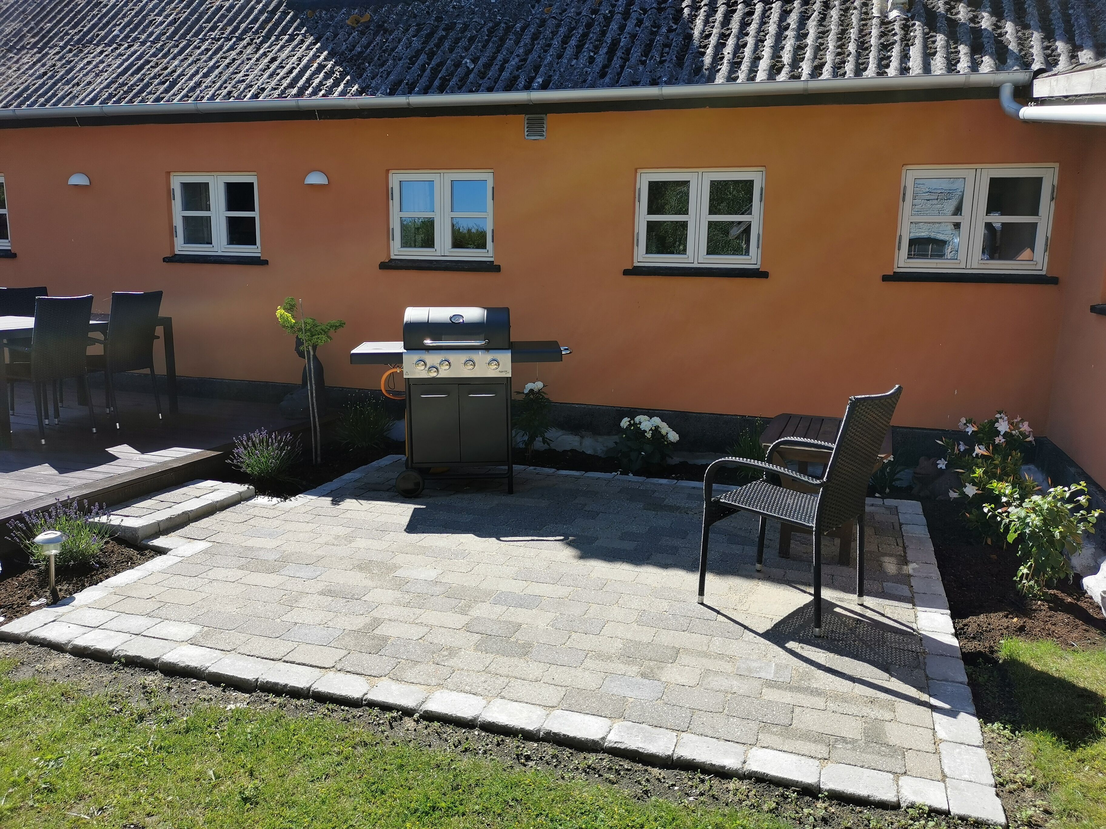 A patio with a grill, outdoor seating, and a house with orange walls and tiled roof.
