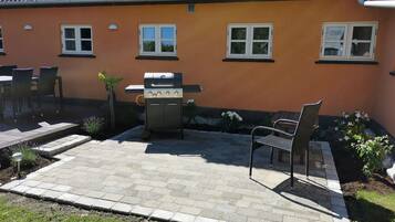 A patio with a grill, outdoor seating, and a house with orange walls and tiled roof.