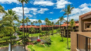Un resort con varias edificaciones, palmeras, un estanque y un césped bien cuidado.