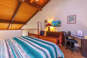 A bedroom with a bed, desk, chair, lamp, and artwork on the wall.