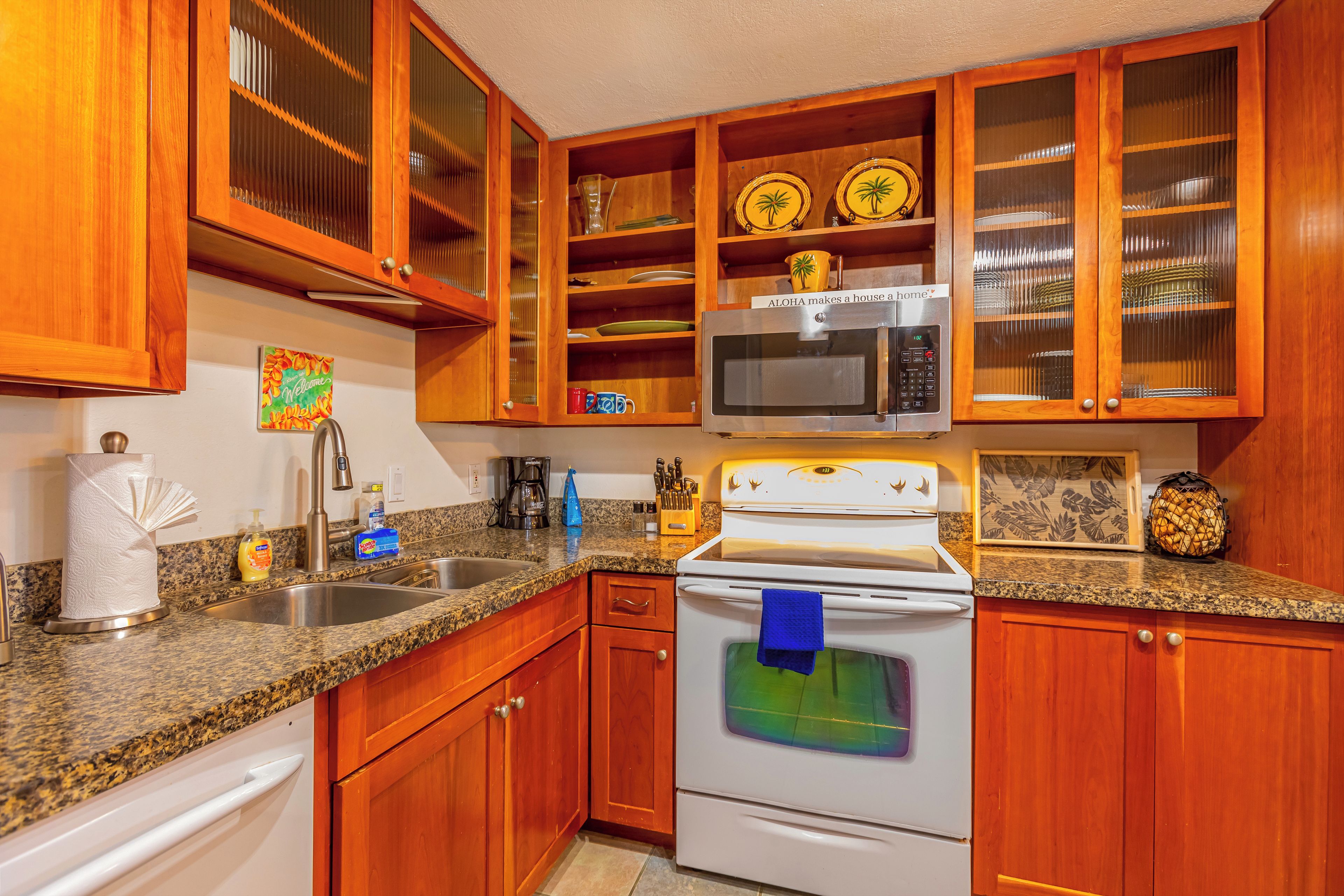 A kitchen with wooden cabinets, a granite countertop, a microwave, an oven, and a sink.
