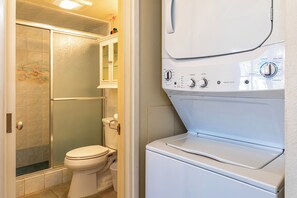 A compact bathroom with a walk-in shower, toilet, and a front-loading washer.