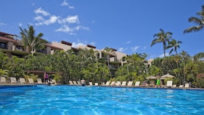 Una piscina con sillas de descanso y palmeras, rodeada de edificios de hotel.