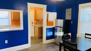 A kitchen with blue walls, wooden cabinets, a stainless steel refrigerator, and a dining table with chairs. - Royalty Homes - College Style 3 bedroom Apartment (Baltimore)
