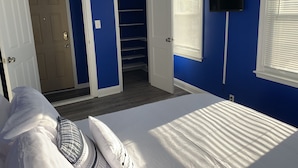 A bedroom with a bed, white pillows, a TV mounted on the wall, and a closet with a sliding door. - Royalty Homes - College Style 3 bedroom Apartment (Baltimore)