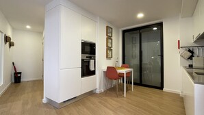 Una cocina moderna con electrodomésticos integrados, un comedor con mesa y sillas, y un puerta corrediza de vidrio que da a otra habitación.