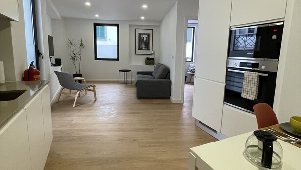 Una cocina moderna con horno y microondas integrados, un comedor con mesa y sillas, y una sala de estar con sofá y una planta.