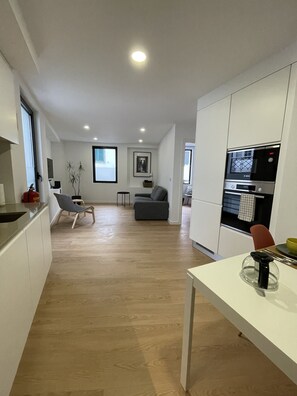 A modern kitchen with a built-in oven and microwave, a dining area with a table and chairs, and a seating area with a sofa and a plant. - Living PDL 2, new and contemporary apartment in the center of Ponta Delgada (Ponta Delgada)