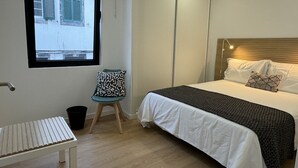 Un dormitorio con cama, una silla, un ventanal y una puerta.