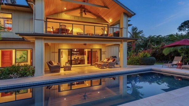 Une maison à deux étages avec piscine, comprenant un grand espace de vie ouvert, aménagé avec des meubles et doté d’un ventilateur de plafond.