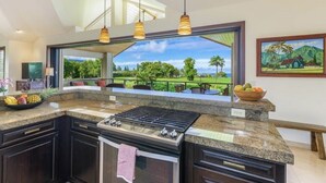 Une cuisine dotée d’un grand îlot central, d’une cuisinière à gaz et offrant une vue sur un paysage luxuriant.