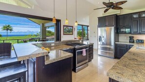 Une cuisine moderne avec des meubles de couleur sombre, des appareils électroménagers en acier inoxydable et un grand îlot central.