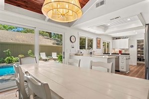 A modern kitchen with white cabinetry, a dining area with a large table, and a view of a backyard with a pool.