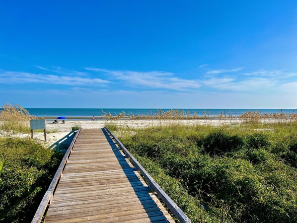 A wooden boardwalk leading to a beach with clear skies.