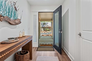 A hallway with a wooden bench, a woven basket, a glass door leading outside, and a decorative wall piece.