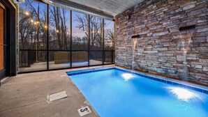 An indoor swimming pool with a stone wall and large windows overlooking trees. - Your own pool! Sauna, Theater, Top 1% (Gatlinburg)