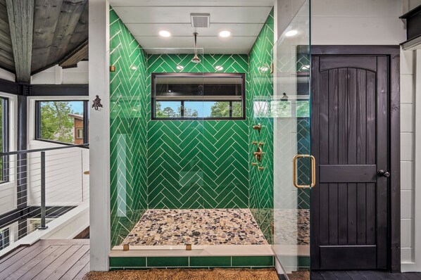 Een moderne badkamer met een groene wand van visgraat tegels, een raam en een douchegedeelte met een vloer van kiezelstenen.