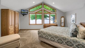 A bedroom with a sloped ceiling, large windows, a bed with patterned bedding, a wooden wardrobe, and a television on the wall. - Sandy Shore Beach House:  Lake Minnetonka (Mound)